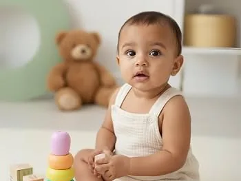 A baby sitting beside a pastel stacking-ring toy and wooden blocks